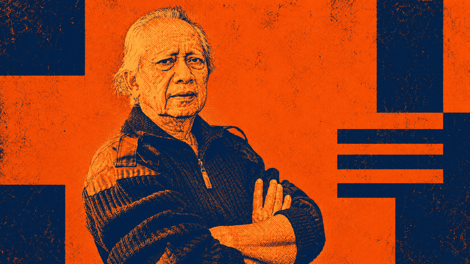 Kakek dengan ekspresi serius dan tangan bersilang, mengenakan jaket di latar belakang berwarna orany.